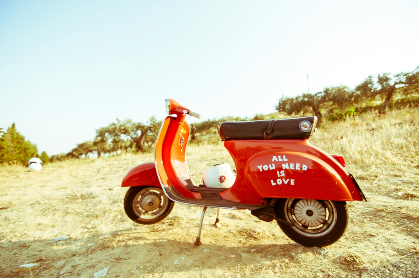 Red and black motor scooter in an open field under a clear blue sky